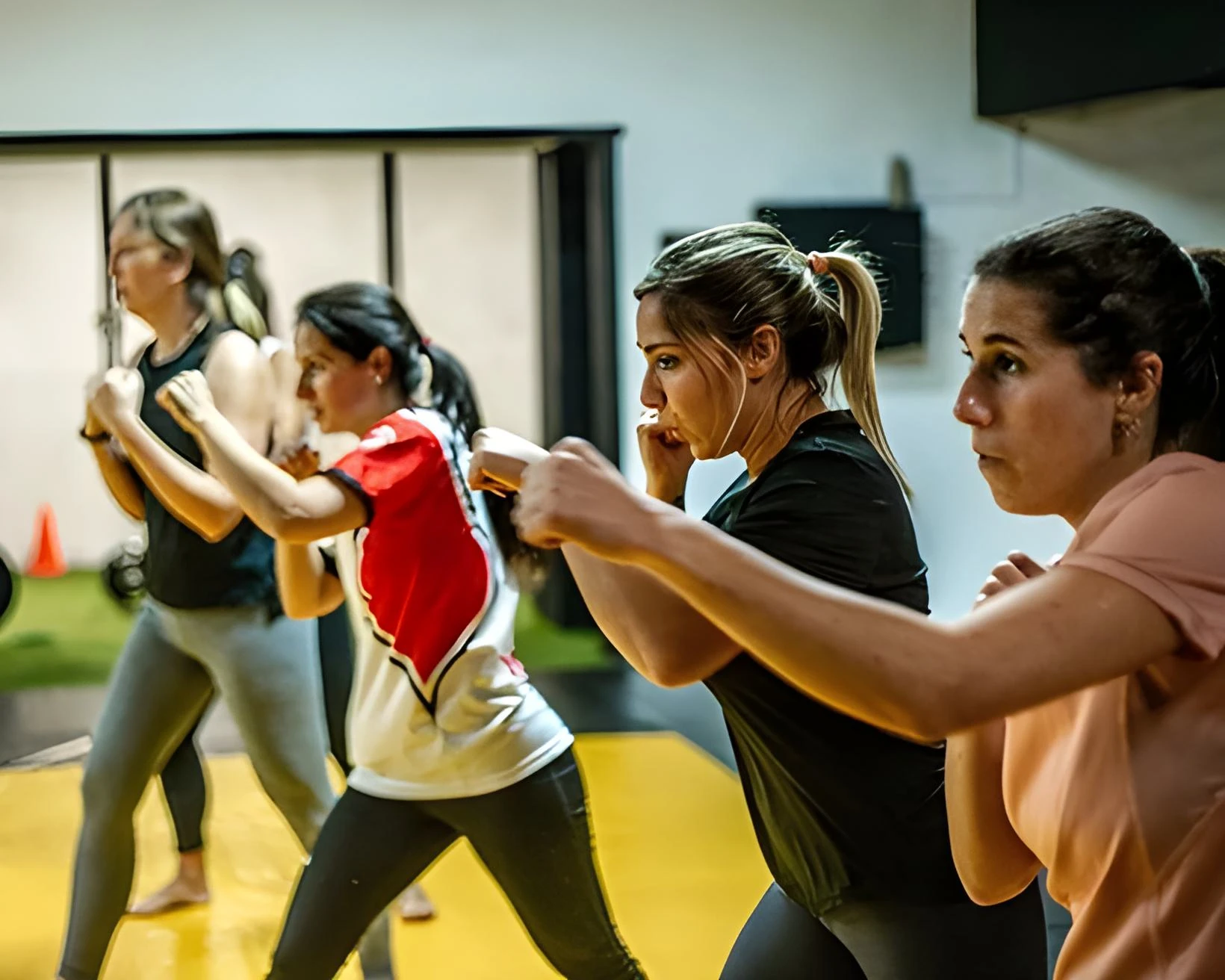 Grupo de mujeres empoderadas entrenando artes marciales en un ambiente de apoyo y respeto mutuo. Las mujeres están en posición de combate, mostrando confianza y determinación.